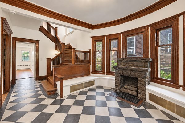 The foyer: checkerboard floor, stone fireplace, built-in window seats and the turned-baluster staircase