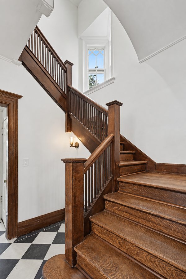 The grand turned-baluster staircase rising from the checkerboard floor